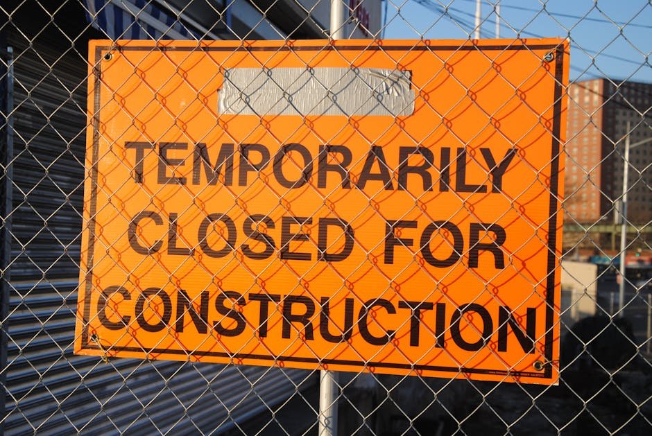 Orange sign behind fence reading 'Temporarily Closed for Construction' at site.